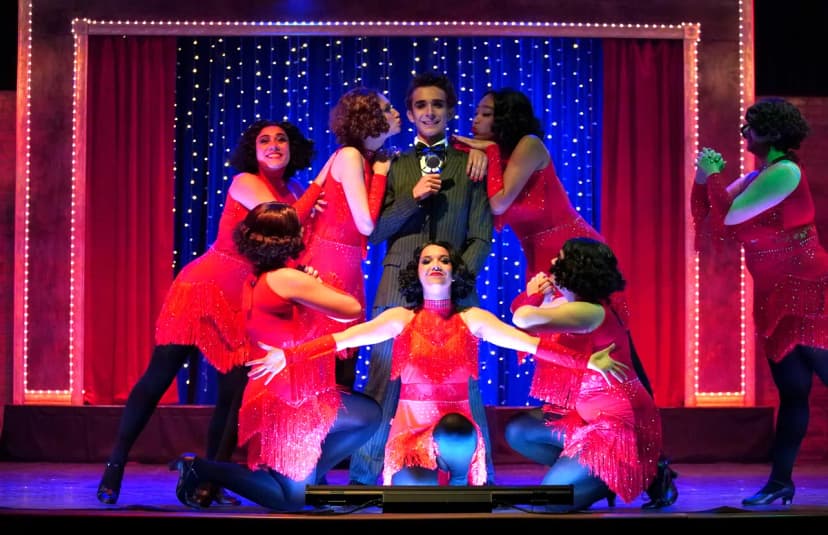 A moment from chicago show, students in red dresses and one male students in the middle dressed in a suit 